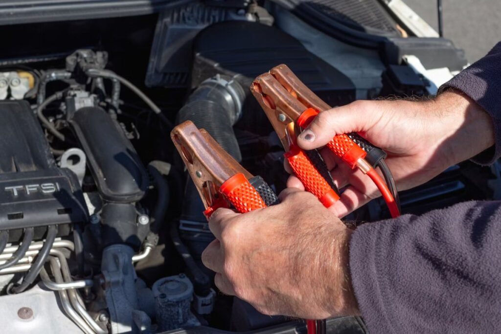 Person holding red and black jumper cables next to a car