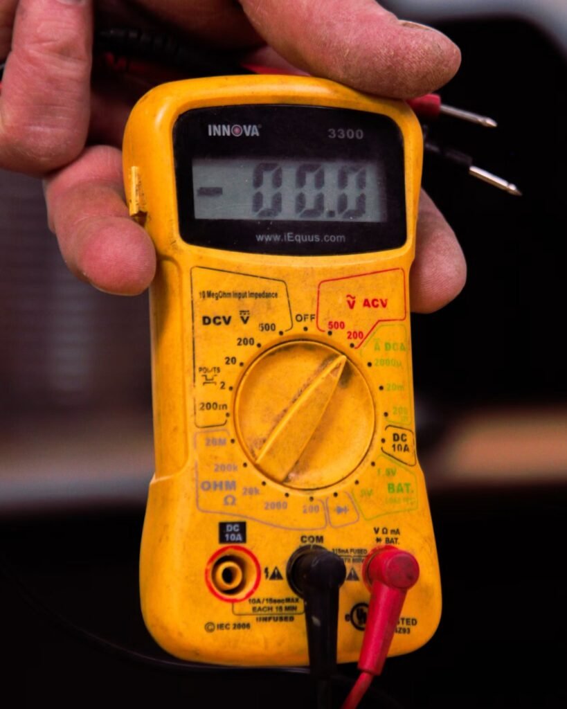 Person holding a digital multimeter to test car battery voltage