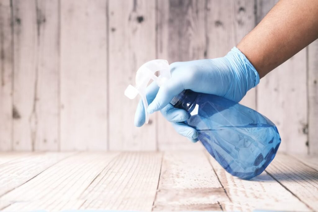Gloved hand holding a spray bottle of vinegar solution for cleaning shower glass