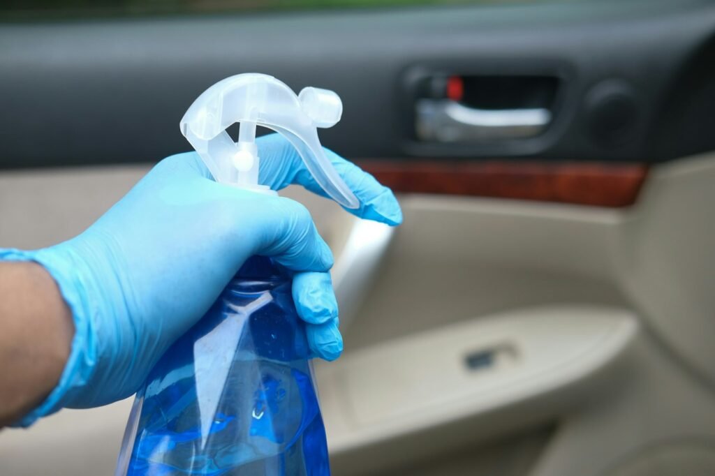 Gloved hand holding a spray bottle while cleaning the inside of a car