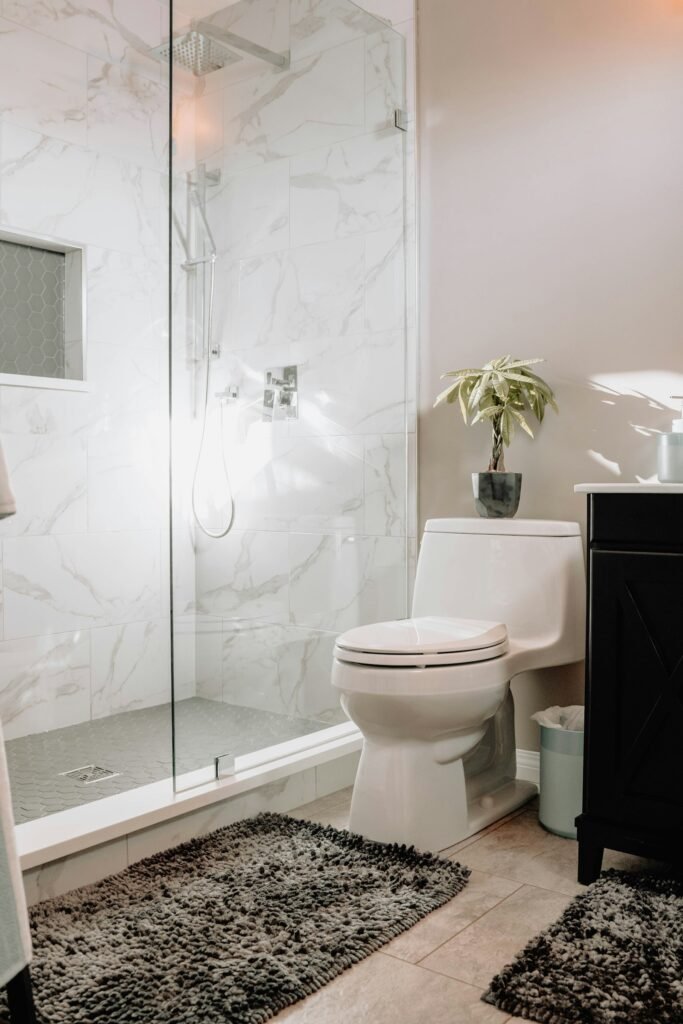 Toilet next to a glass shower in a bright marble-tiled bathroom