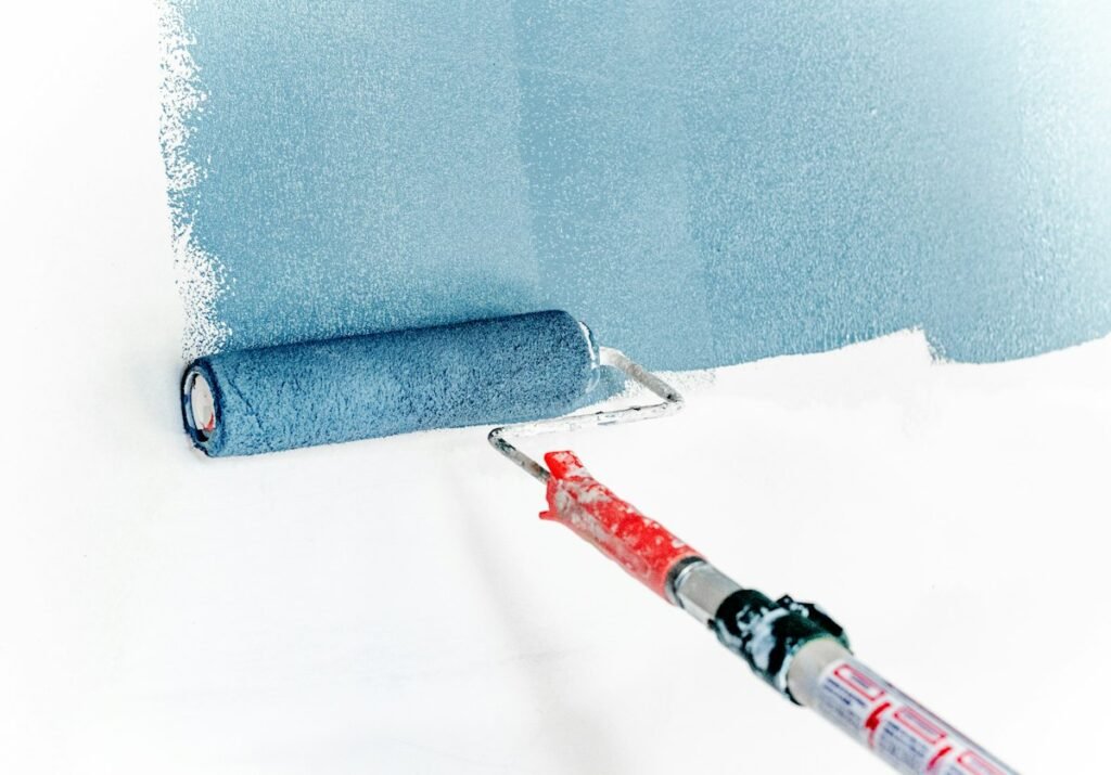 Paint roller applying blue paint to a clean wall after glue removal