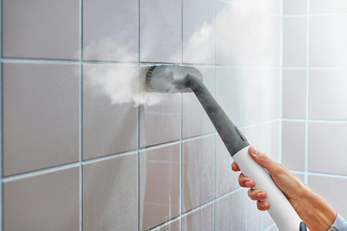 Steam cleaner cleaning a tiled bathroom wall
